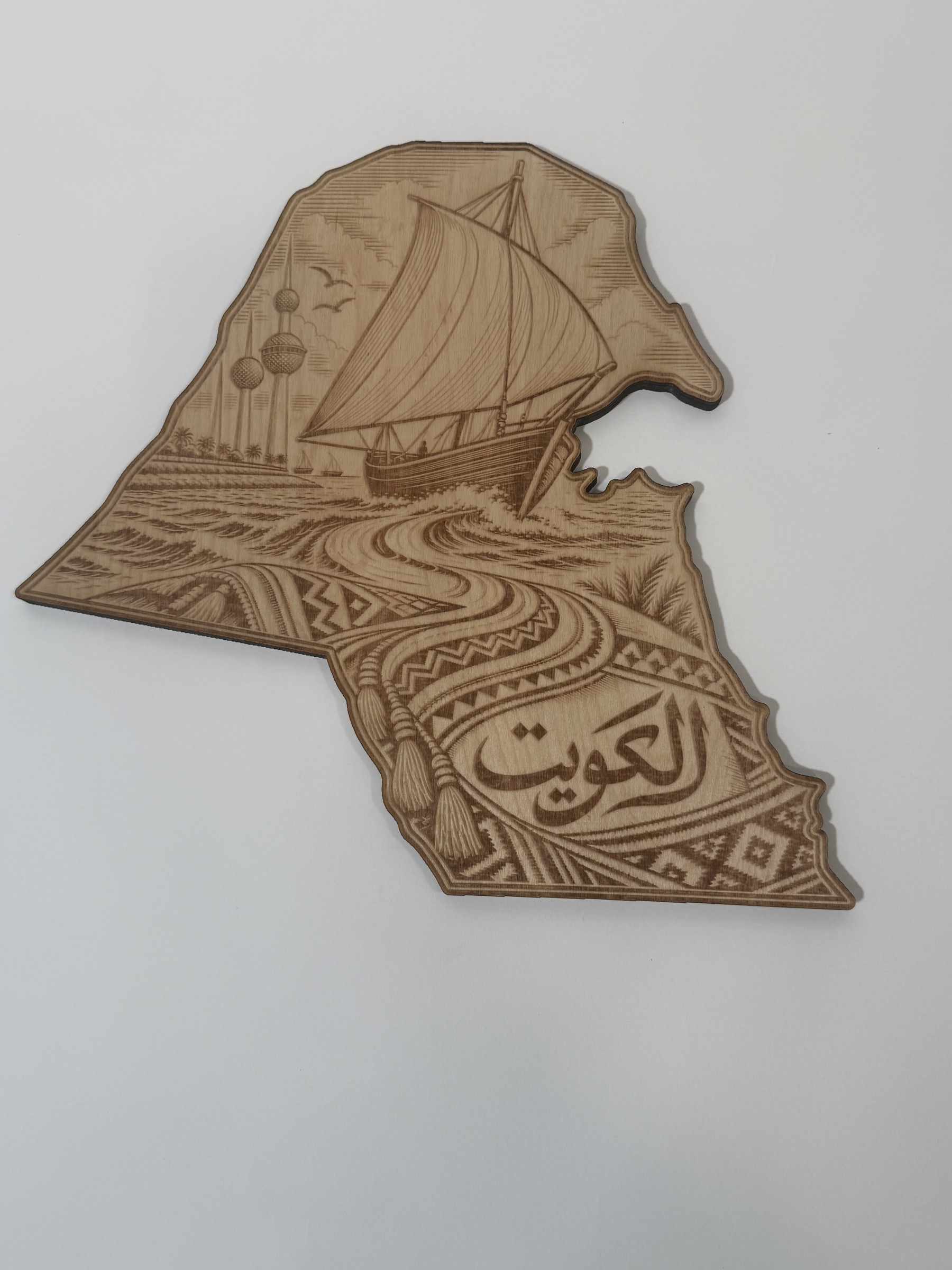 Real product photograph of Kuwait wood wall art, showing a dhow, Kuwait Towers, waves, patterned cloth and الكويت and natural wood grain.