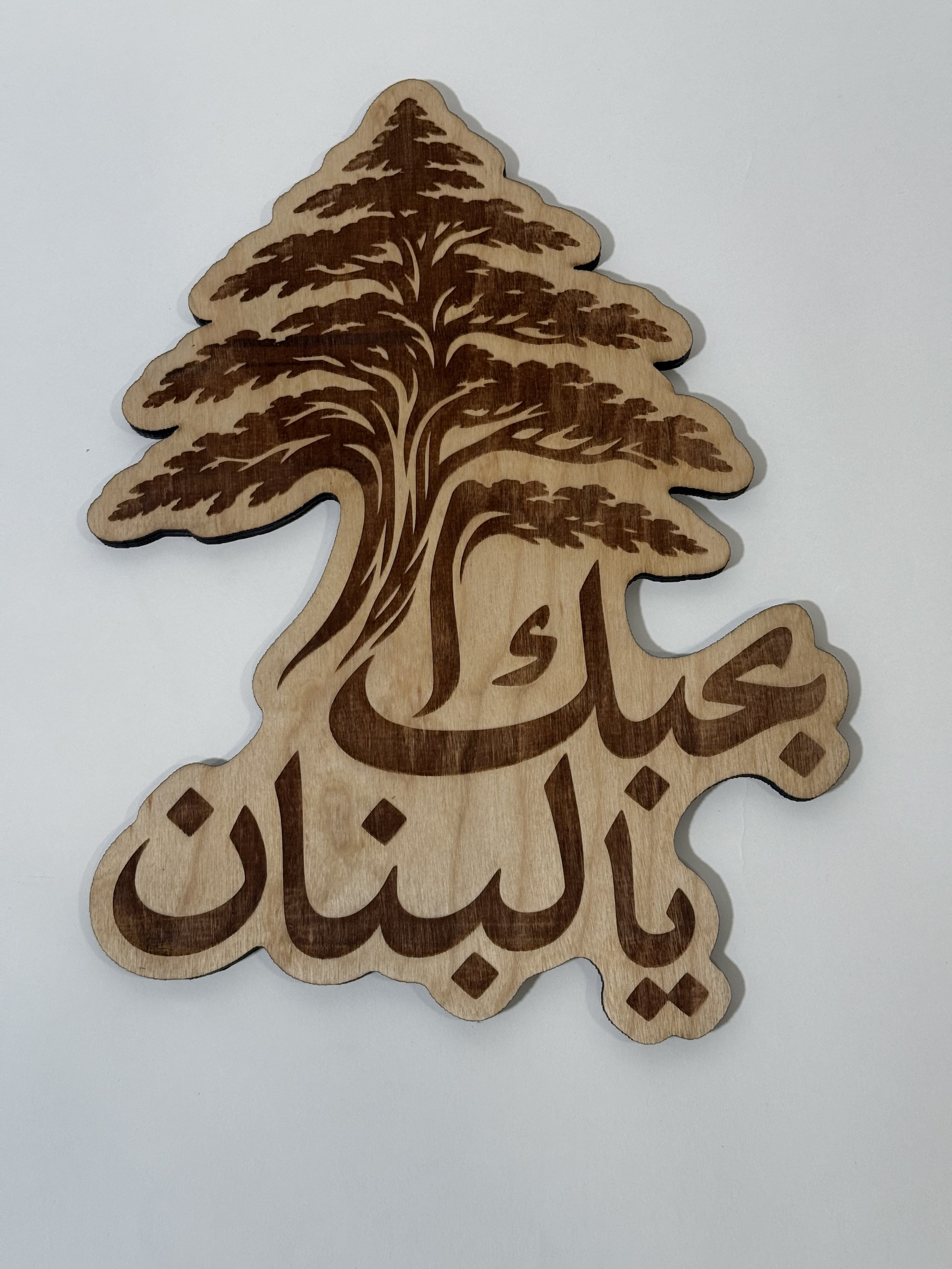 Real product photograph of Lebanon wood wall art, showing a cedar tree flowing into the Arabic phrase بحبك يا لبنان and natural wood grain.