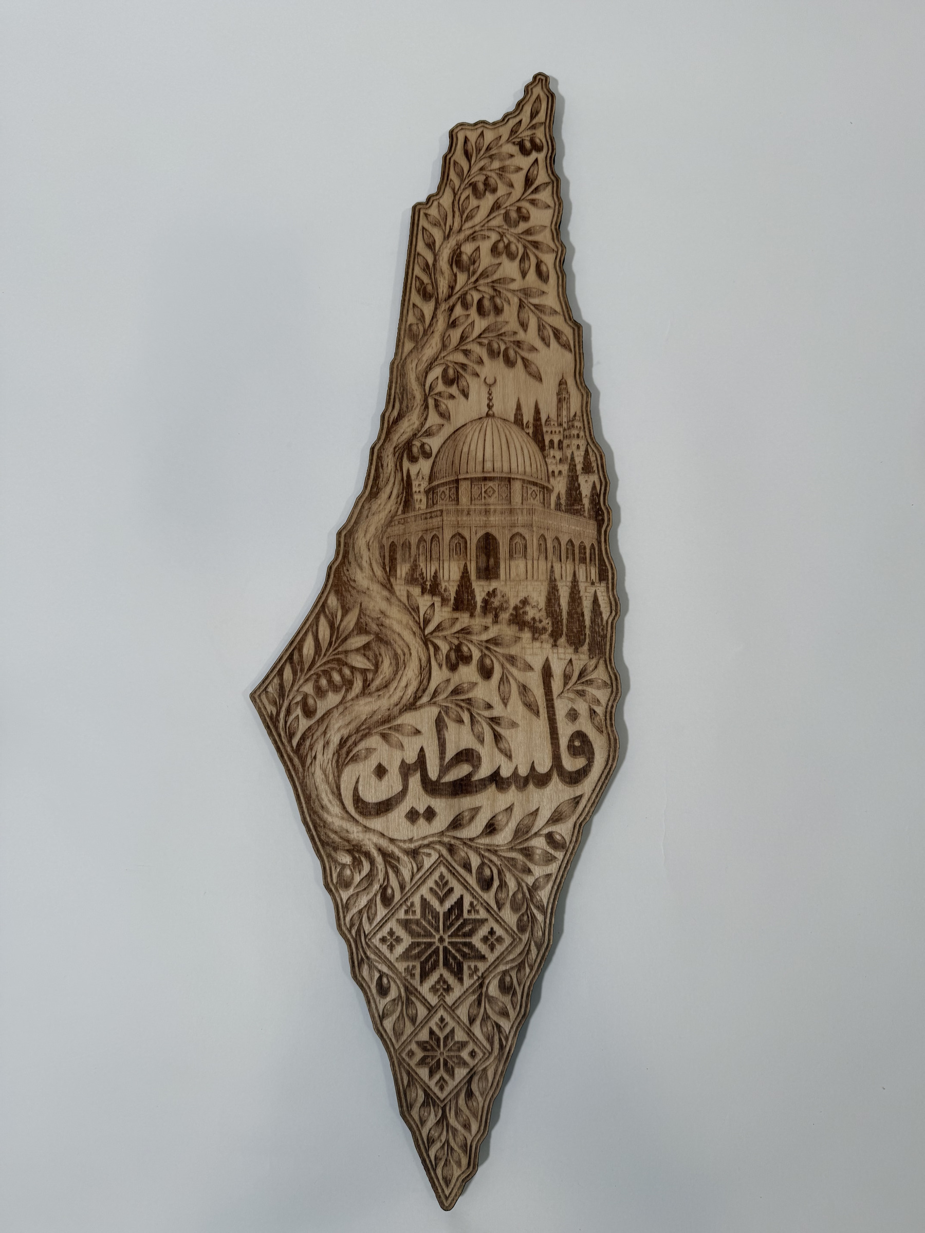 Real product photograph of Palestine wood wall art, showing an olive tree, the Dome of the Rock, geometric floral diamonds and فلسطين and natural wood grain.