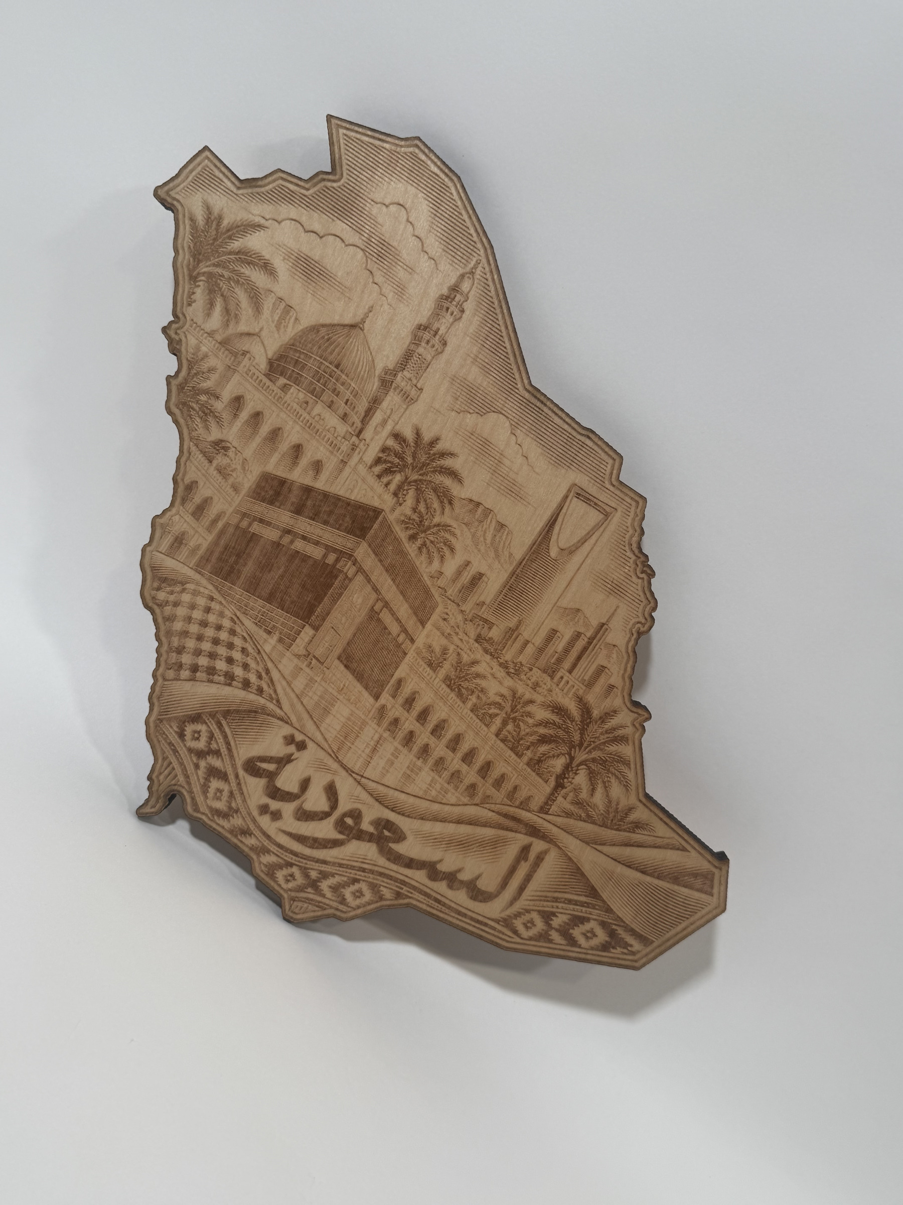 Real product photograph of Saudi Arabia wood wall art, showing the Kaaba, mosque architecture, palms, a skyline tower and the Arabic name السعودية and natural wood grain.